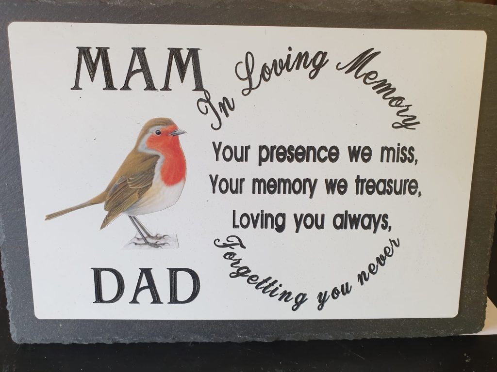 A picture of a personalised 'in memorial' plaque. It features of a picture of a robin centered between the text of "Mam and Dad". The message reads "In Loving Memory. Your presence we miss, your memory we treasure, Loving you always, Forgetting you never